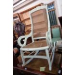 A later white painted antique scroll arm rocking chair with rattan back and seat panels