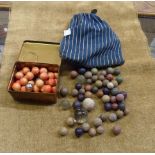 A bag and a tin containing a quantity of old clay marbles