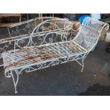 A white painted wrought iron chaise longue form garden bench with decorative scroll back and