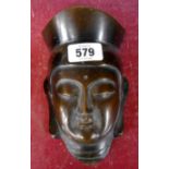 A vintage cast iron wall mask depicting a buddha with bronzed finish