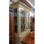 A 1.1m shabby chic painted wood two part book cabinet with astragal glazed top over a base with pair