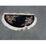 A semi circle shaped machine made rug with florals motifs on black ground