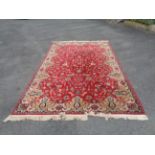 A large machine made rug with floral pattern on red ground within decorative border - 3.1m X 1.95m