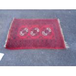 A small handmade rug with black and white octagonal emblems on red ground -a/f