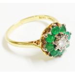 An 18ct. gold flowerhead pattern ring, set with central diamond within an eight stone emerald