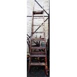 An antique tall stepladder with decorative cast iron brackets and shaped finials