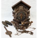 An old Black Forest stained and carved wood cuckoo wall clock with twin pinecone pattern weights -