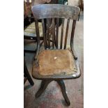An old oak lathe back office swivel chair with remains of studded leather upholstery, set on
