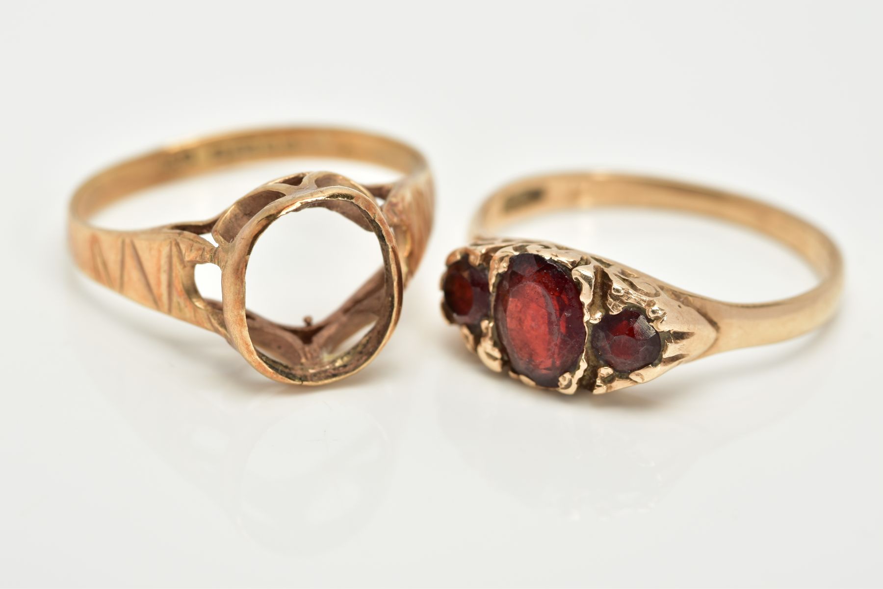 TWO 9CT GOLD RINGS, the first a graduated three stone oval cut garnet ring, within a scroll detailed