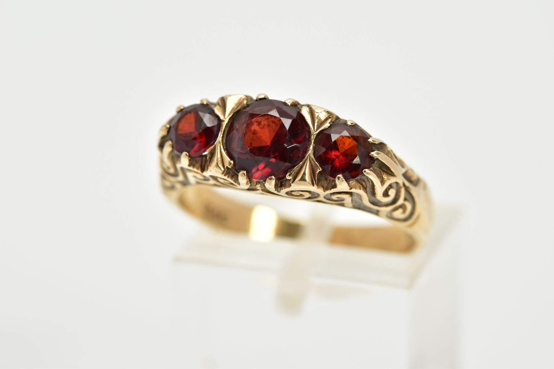 A 9CT GOLD THREE STONE GARNET RING, set with three graduated circular cut garnets, within a scroll