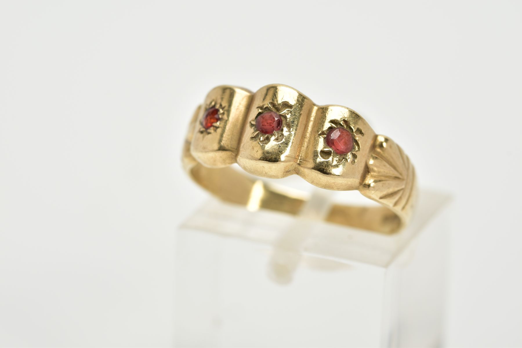 A 9CT GOLD GARNET RING, designed with three curved sections, each set with a circular cut garnet, to