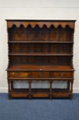 A REPRODUCTION OAK DRESSER the top with a wavy apron above the plate rack shelves the base with