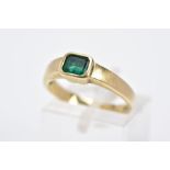 A YELLOW METAL EMERALD RING, the emerald cut within a collet mount to the plain polished band,