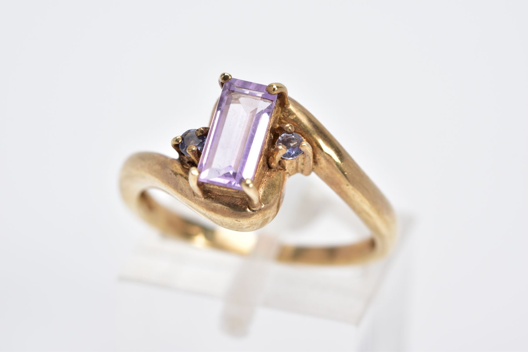 A 9CT GOLD AMETHYST RING, of cross over design, set with a central rectangular cut amethyst