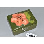 A MOORCROFT POTTERY RECTANGULAR TRINKET BOX AND COVER, the lid with a coral hibiscus, on a green