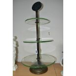 AN EARLY 20TH CENTURY THREE TIER GLASS ADVERTISING DISPLAY STAND, the iron and worn brassed stand