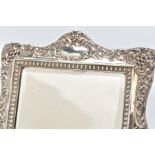 AN EDWARDIAN SILVER FRAMED MIRROR, of an embossed foliate and scroll design with a vacant cartouche,