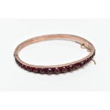 A ROSE GOLD PLATED HINGED BANGLE, set with rose cut red and orange garnets all round, fitted with