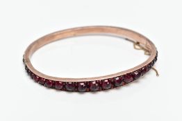 A ROSE GOLD PLATED HINGED BANGLE, set with rose cut red and orange garnets all round, fitted with