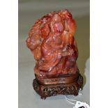 AN ORIENTAL CARVED ORANGE HARDSTONE FIGURE OF A DEITY, holding a jar in one hand with smoke