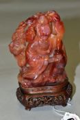 AN ORIENTAL CARVED ORANGE HARDSTONE FIGURE OF A DEITY, holding a jar in one hand with smoke