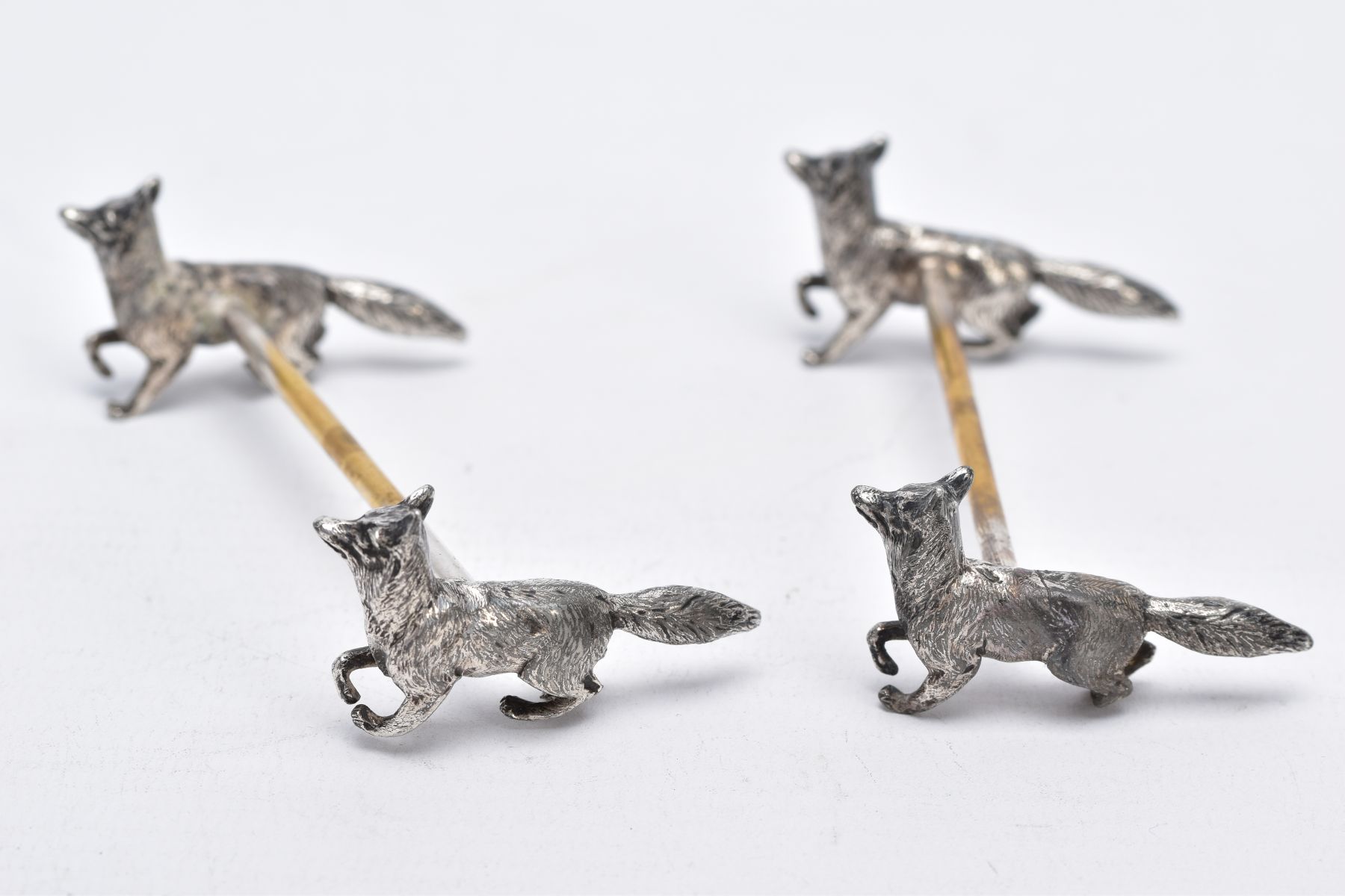 A PAIR OF WHITE METAL KNIFE RESTS, each rest modelled with two foxes to each end with a worn gilt