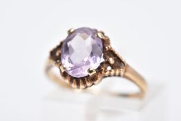 A 9CT GOLD AMETHYST RING, designed with a central claw set, oval cut amethyst within a bead and