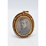 A YELLOW METAL PORTRAIT PENDANT, of an oval form, holding a photo of a gentleman, within a