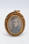 A YELLOW METAL PORTRAIT PENDANT, of an oval form, holding a photo of a gentleman, within a