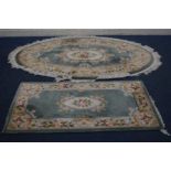 A CHINESE WOOLLEN GREEN OVAL RUG, 220cm x 127cm along with a similar smaller rug, 155cm x 79cm (2)