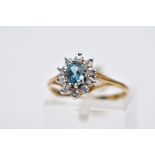 A YELLOW METAL CLUSTER RING, designed with a central oval cut blue topaz, within a circular cut