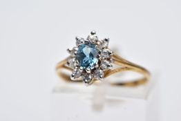 A YELLOW METAL CLUSTER RING, designed with a central oval cut blue topaz, within a circular cut