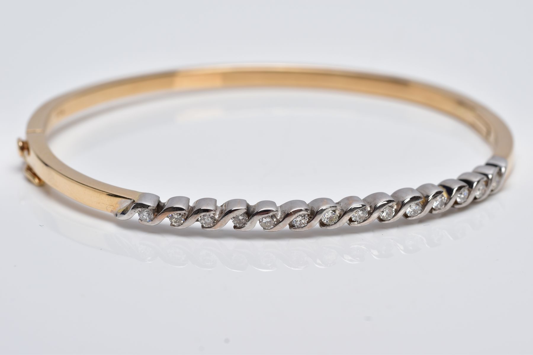 A YELLOW METAL DIAMOND BANGLE, the hinged bangle designed with a row of crossover mounted round