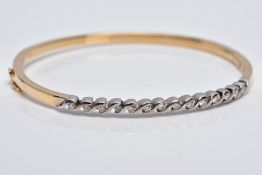 A YELLOW METAL DIAMOND BANGLE, the hinged bangle designed with a row of crossover mounted round