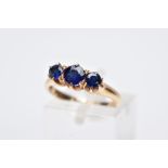 A YELLOW METAL THREE STONE RING, designed with three graduated circular cut blue stones assessed