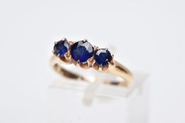 A YELLOW METAL THREE STONE RING, designed with three graduated circular cut blue stones assessed