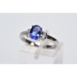 A TANZANITE AND DIAMOND PLATINUM RING, designed with a central claw set, oval cut tanzanite,