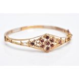 A 9CT GOLD GARNET HINGED BANGLE, of a floral and beaded openwork design, the central flower set with