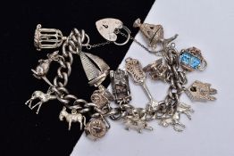 A HEAVY SILVER CHARM BRACELET, suspending fifteen white metal charms in various forms such as a bird