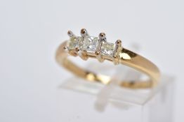 A YELLOW METAL THREE STONE DIAMOND RING, designed with a raised row of three claw set princess cut