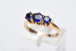 A YELLOW METAL THREE STONE RING, designed with three graduated circular cut blue stones assessed