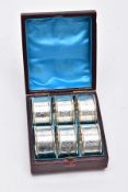 A CASED SET OF SIX SILVER NAPKIN RINGS, each with a decorative foliate and scroll detail with an