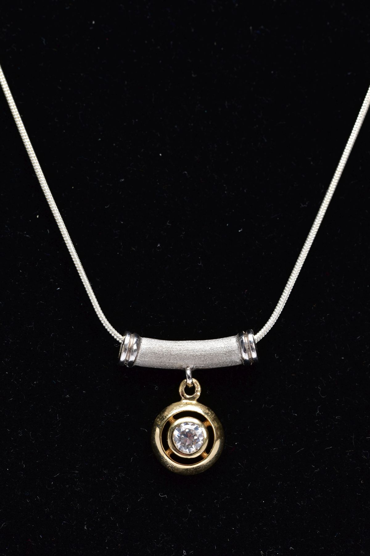 A TWO-TONE PENDANT ON A WHITE METAL CHAIN, the pendant designed with an openwork, circular yellow