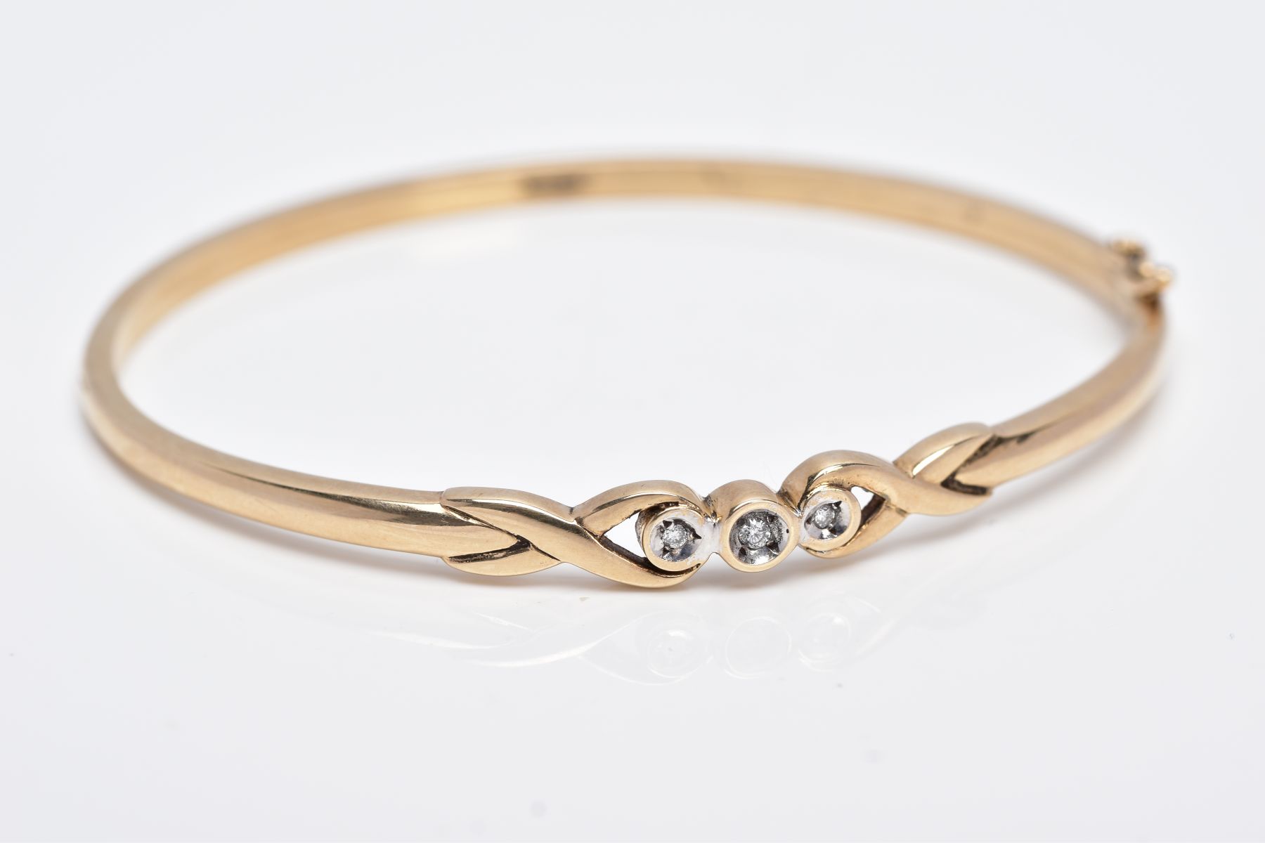A 9CT GOLD DIAMOND BANGLE, designed with a crossover section set with three round brilliant cut