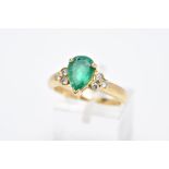 A YELLOW METAL EMERALD AND DIAMOND RING, designed with a central claw set, pear cut emerald, flanked