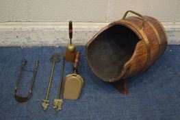 A COOPERED LOG BUCKET, tilted on a stand, along with five various brass fire irons (6)
