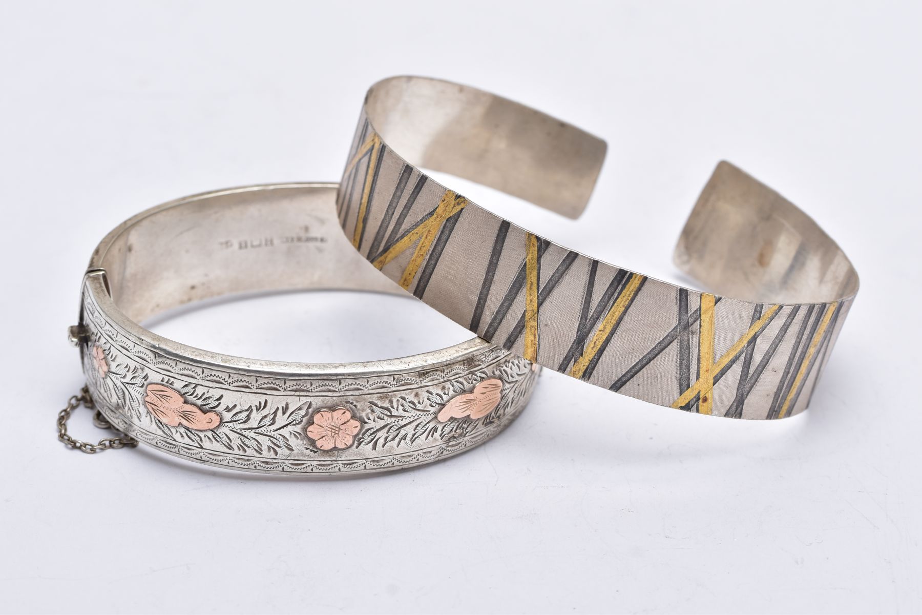 A SILVER BANGLE AND A WHITE METAL CUFF, the silver hinged bangle, with a decorative rose gold tone