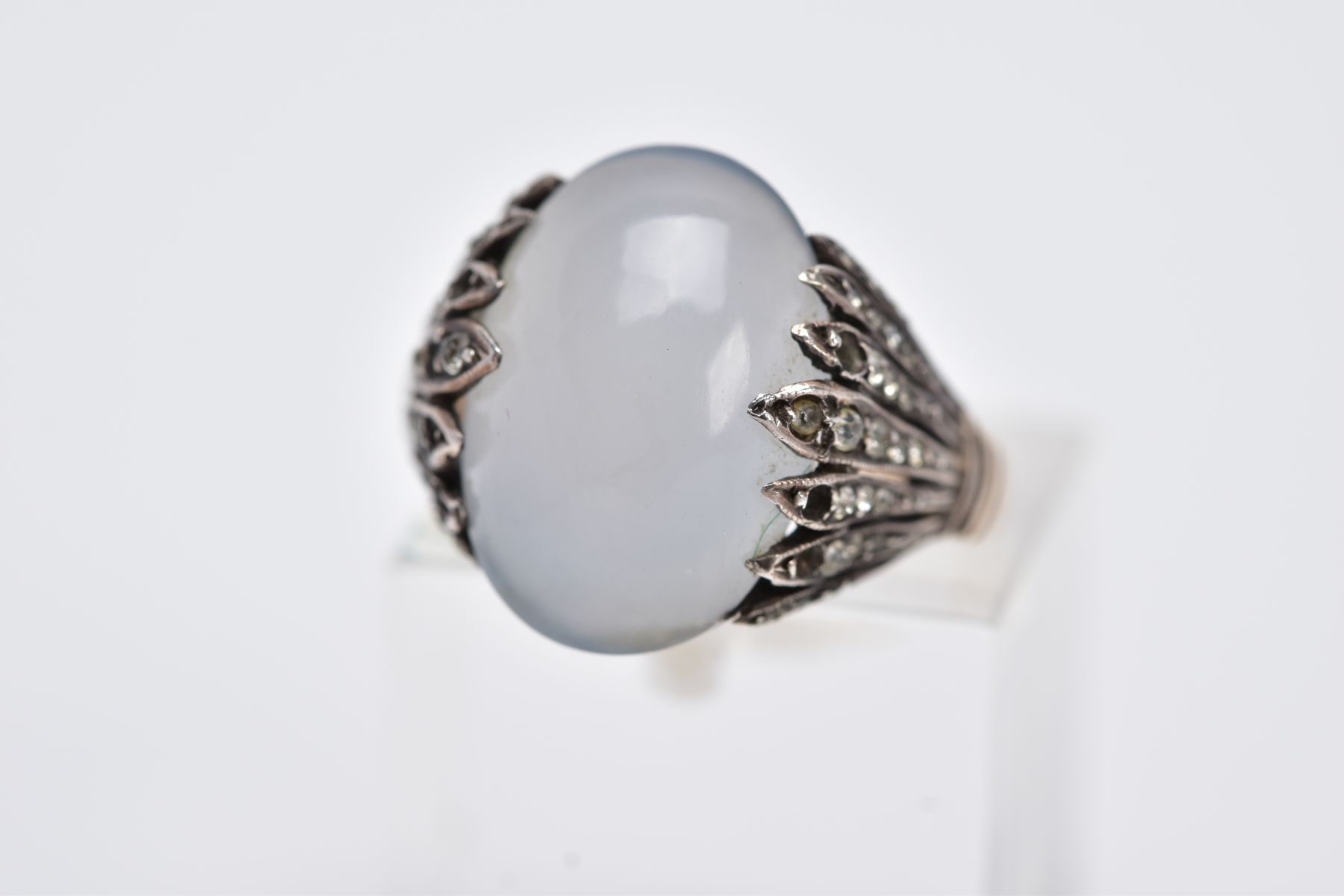 A YELLOW METAL GEM SET RING, designed with a milky chalcedony cabochon, openwork feathered shoulders