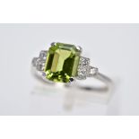 A WHITE METAL PERIDOT AND DIAMOND RING, designed with a central claw set, emerald cut peridot,