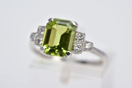A WHITE METAL PERIDOT AND DIAMOND RING, designed with a central claw set, emerald cut peridot,